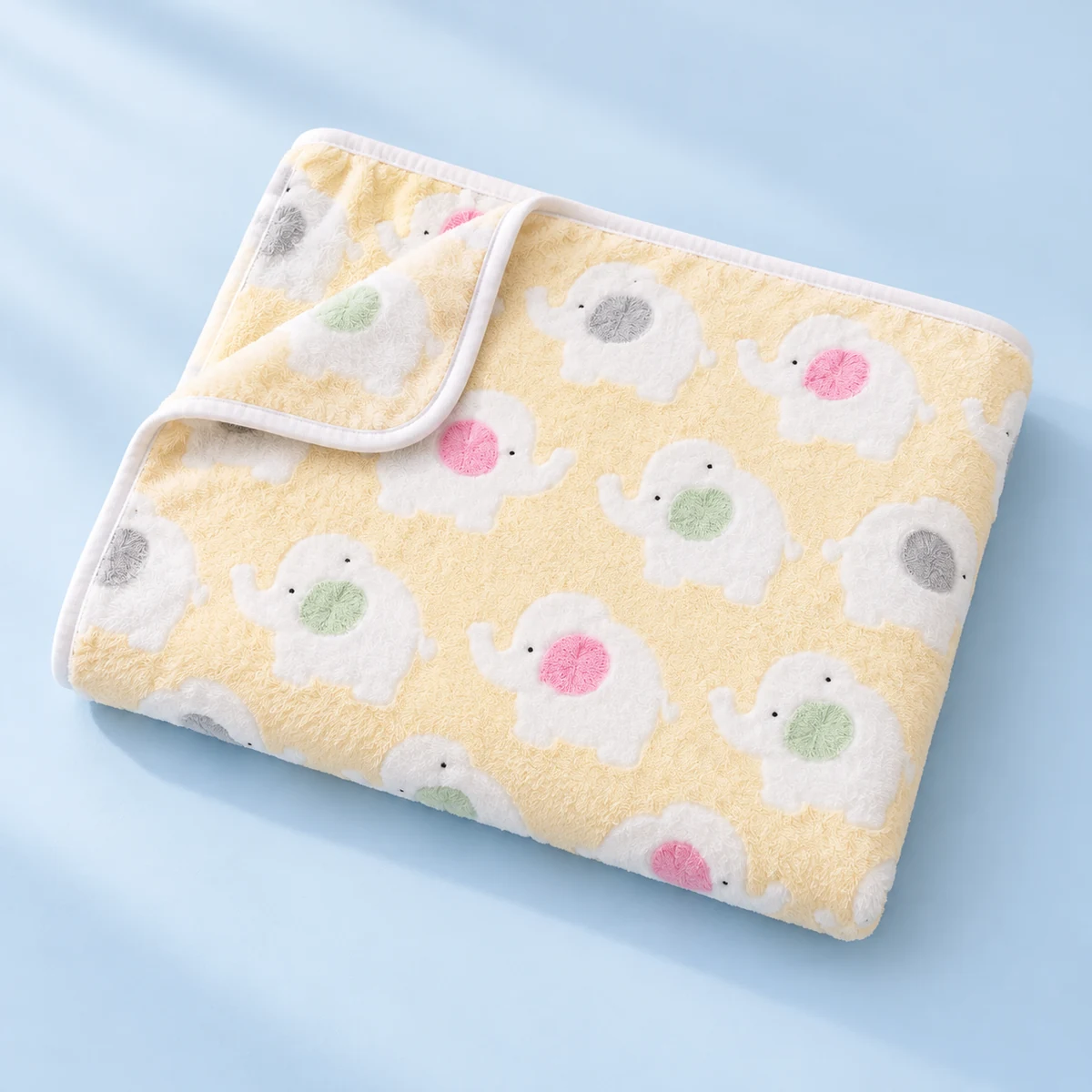 The pale yellow elephant blanket softly folded on a pale blue surface, showing its print and white binding.