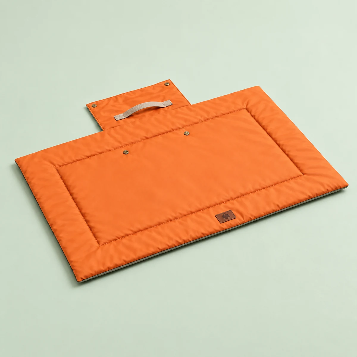 The orange travel mat fully open with its carry flap, beige handle and snap fasteners visible.